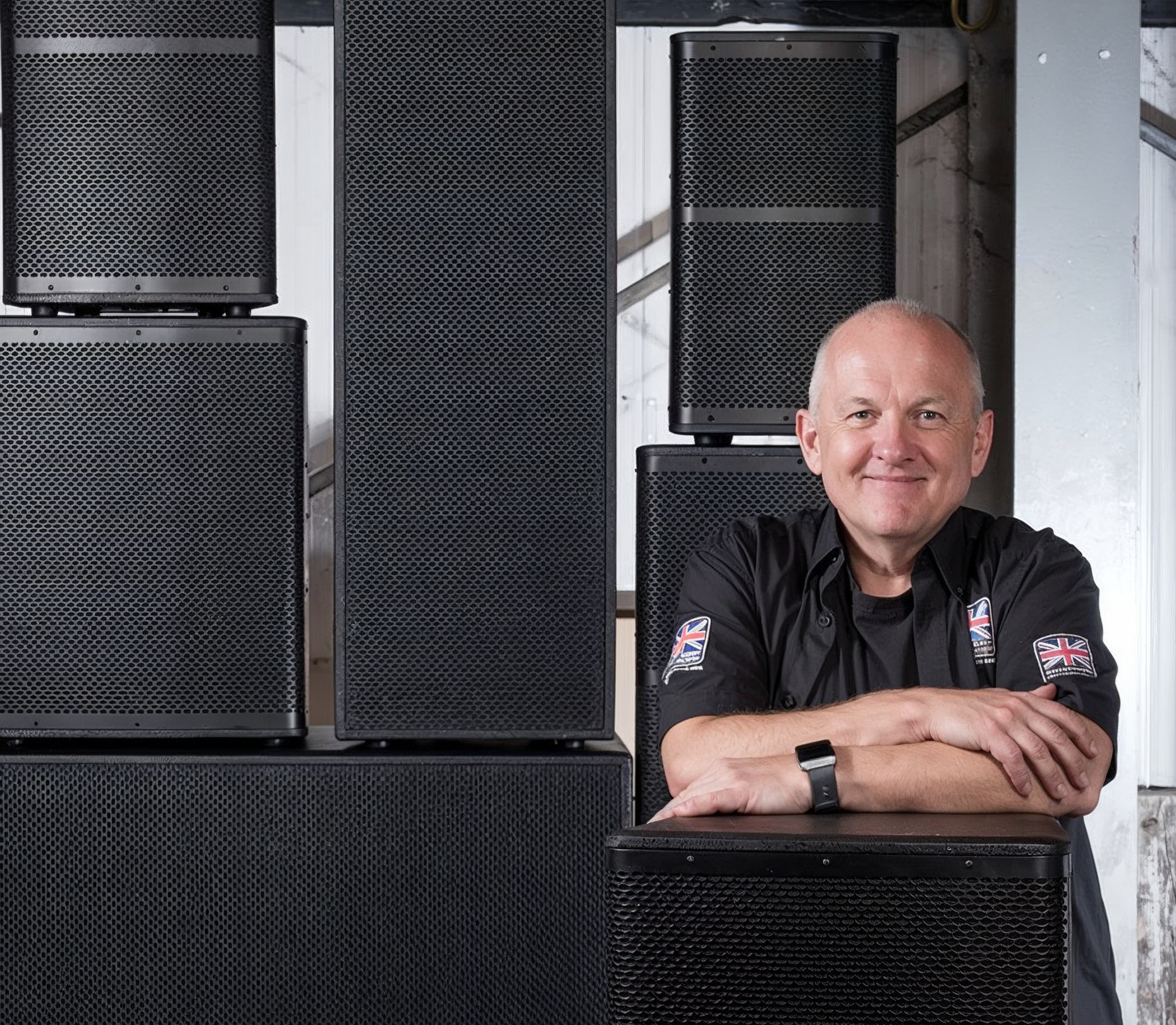 Man standing in front of large black speakers with visible logos on a dark background